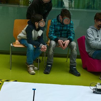 Schüler schauen Studenten über die Schultern wie sie ihre programmierten Roboter auf den weißen mit Linien versehenen Planen fahren lassen.